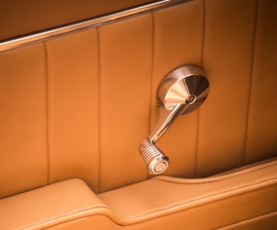 Vintage car's interior showing a chrome door handle and leather upholstery