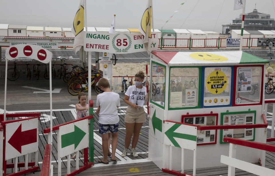 A vendor, asks children to use hand sanitizer before using an amusement ride on the beach at the Belgian seaside resort of Blankenberge, Belgium, Tuesday, Aug. 11, 2020. A skirmish took place on the beach on Saturday, Aug. 8, 2020 which resulted in two coastal communities banning day trippers from the city. (AP Photo/Virginia Mayo)