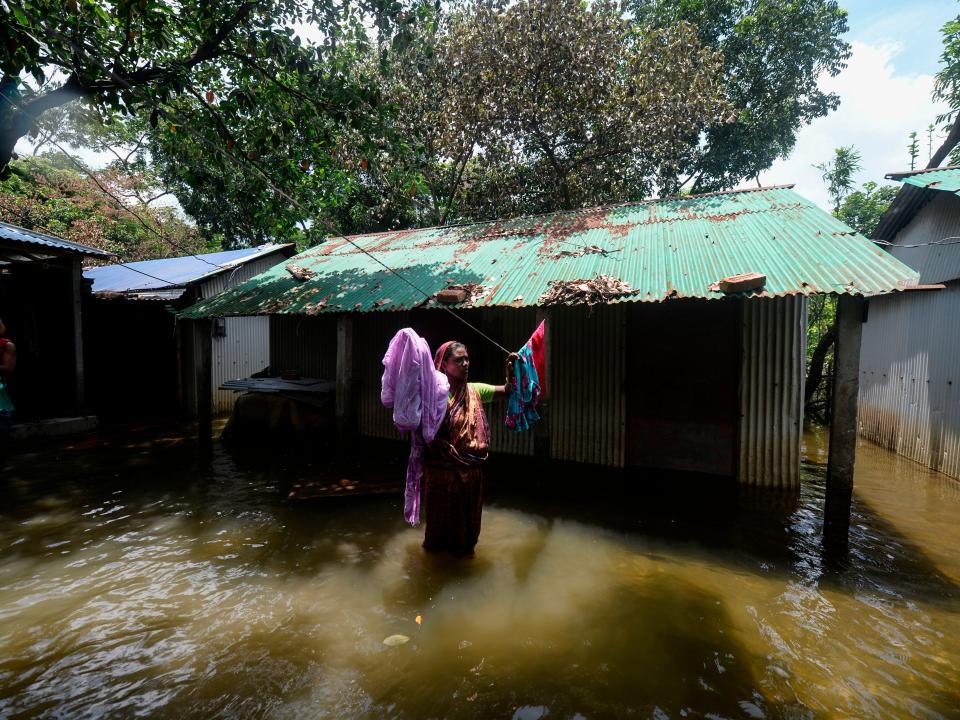 A woman hangs clothes to dry in front of her house in a flooded area due to recent monsoon rainfalls in Dhamrai on August 11, 2020.