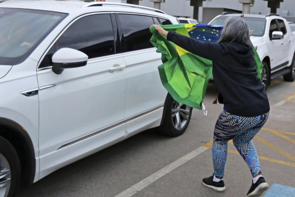 A supporter holds out a Brazilian national flag as the car transporting former Brazilian President Jair Bolsonaro drives by at the international airport in Florianopolis, Santa Catarina state, Brazil, Friday, July 5, 2024. Brazilian police have indicted Bolsonaro for money laundering and criminal association in connection with undeclared diamonds the far-right leader received from Saudi Arabia during his time in office, according to a source with knowledge of the accusations. (AP Photo/Heuler Andrey)