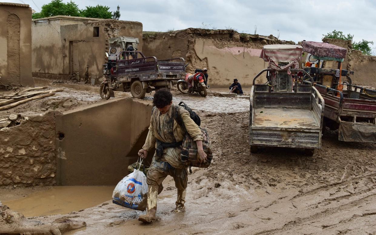 An Afghan man carries his belongings as he walks through a mud-covered street in Laqiha village