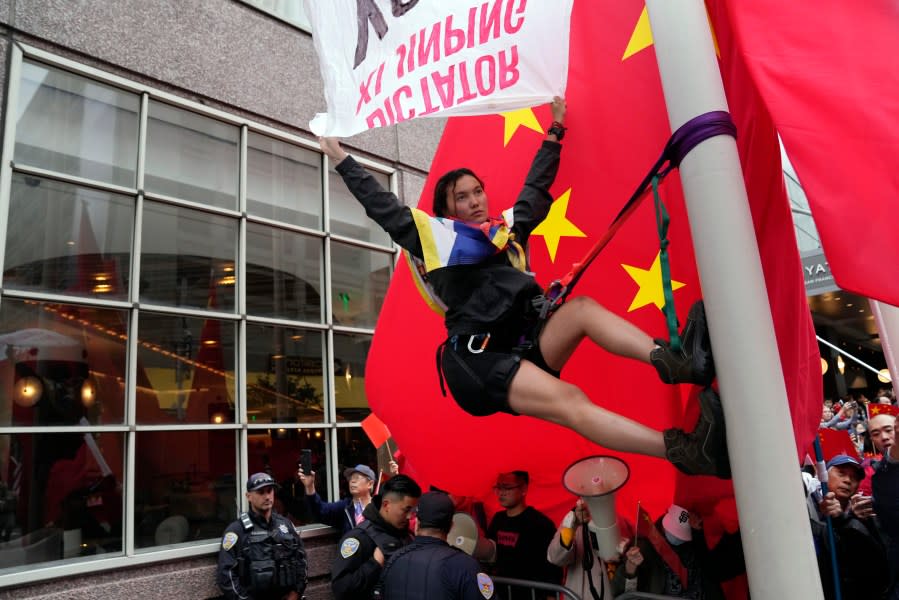 A protester climbs up a pole in front of supporters of Chinese President Xi Jinping near the site of the APEC Summit, Wednesday, Nov. 15, 2023, in San Francisco. (AP Photo/Godofredo A. Vásquez)