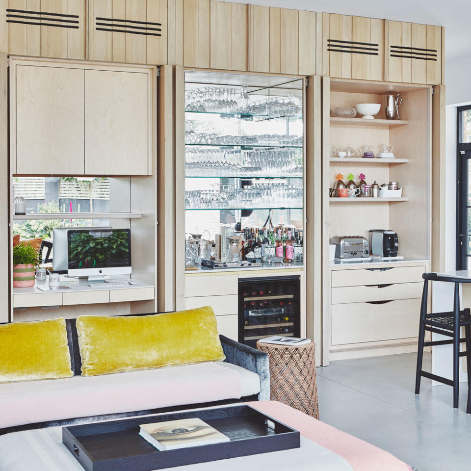 wooden wall mounted cabinet with a mini bar and a desk-area next to a black material sofa