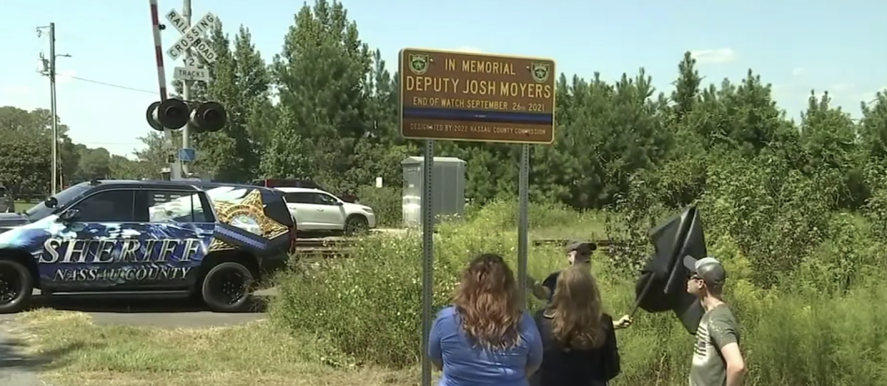 The family of Nassau County Deputy Joshua Moyers, who died one year ago after being shot here on Sandy Ford Road just outside Callahan, watch as a memorial sign is unveiled in his honor Monday.