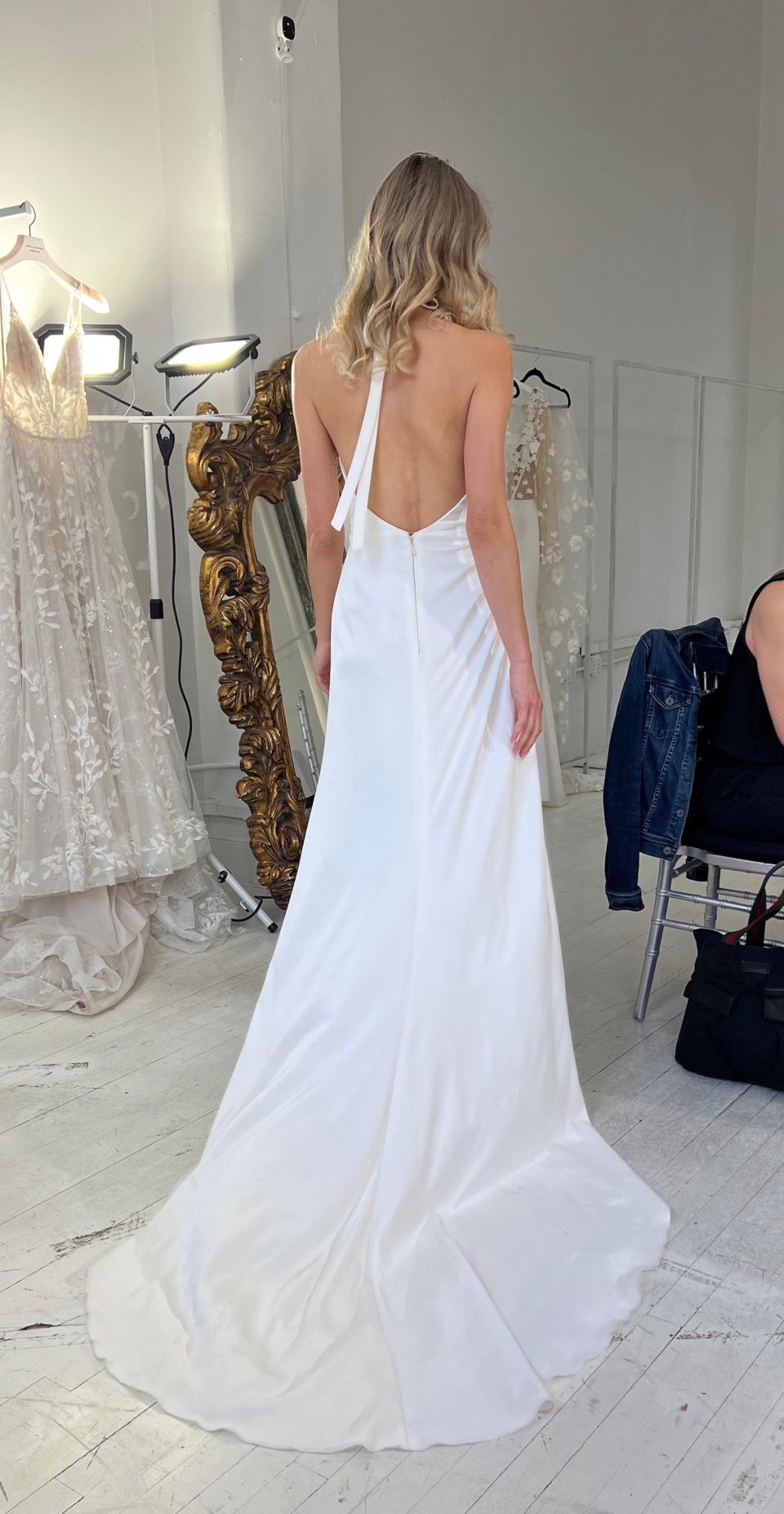 A woman walks through a room, showing off her backless wedding dress.