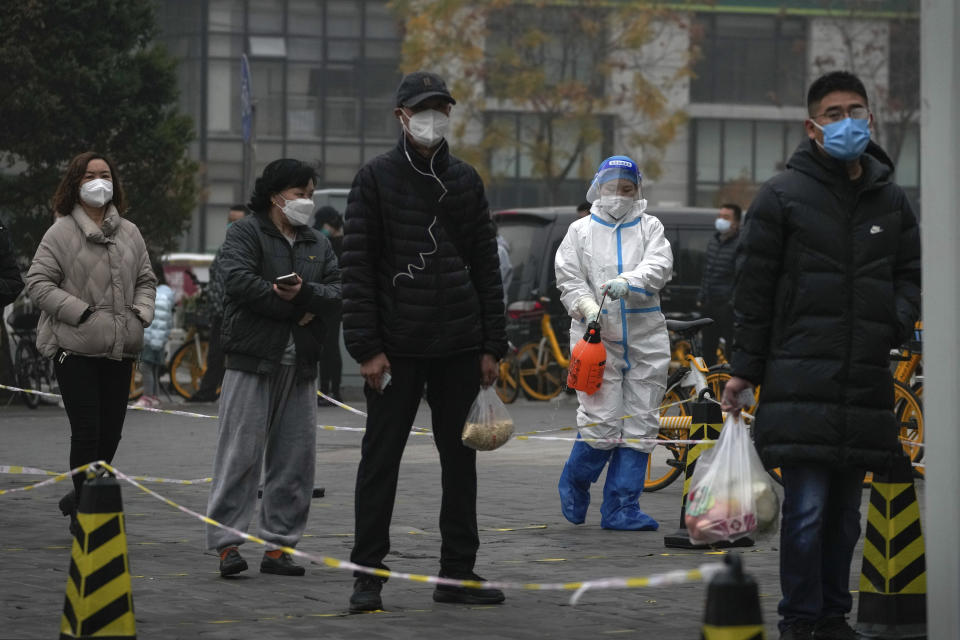 A worker in protective suit sprays disinfectant as residents stand in line for their routine COVID-19 throat swabs at a coronavirus testing site in Beijing, Thursday, Nov. 24, 2022. China is expanding lockdowns, including in a central city where factory workers clashed this week with police, as its number of COVID-19 cases hit a daily record. (AP Photo/Andy Wong)