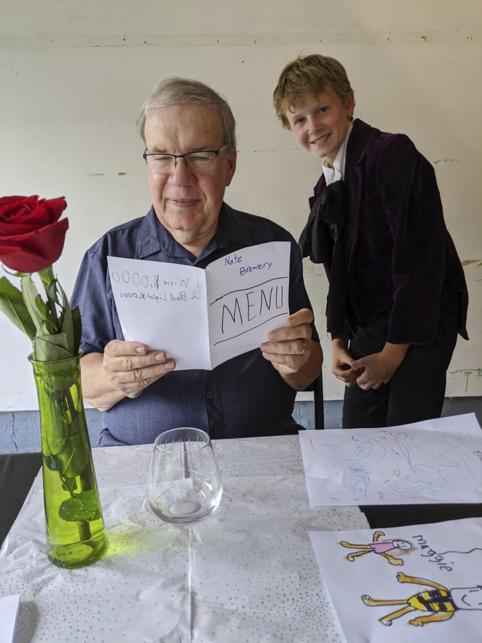 In this Aug, 2020, photo provided by courtesy of Nancy Peters, Joe Peters reads the menu on his birthday in a garage served by grandson, Nate Hoying, right, in Cincinnati. Both Joe and Nancy Peters are retired educators in their 70s who were used to being heavily involved with the grandchildren, all living near them in suburban Cincinnati, before the pandemic and its safety restrictions hit. (Nancy Peters via AP)