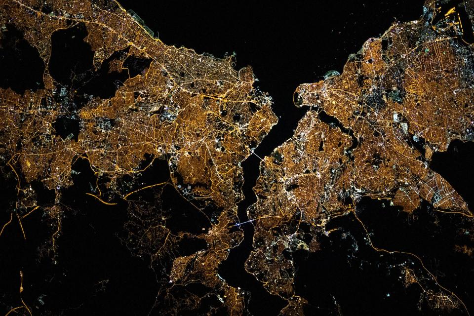 istanbul city grid lit up yellow gold at night with dark ocean waters and river splitting the city as seen from above