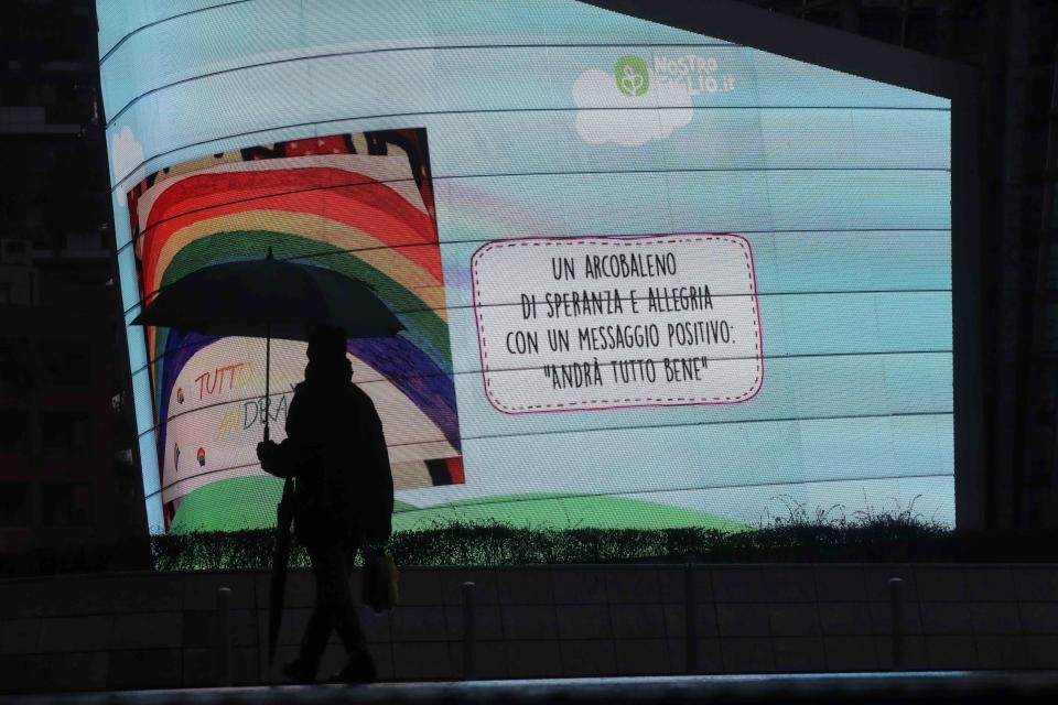 In this photo taken on Saturday, March 14, 2020 a man walks past a billboard reading in Italian "A Rainbow of hope and cheerfulness with a positive message, everything will be alright", in Milan, Italy. The nationwide lockdown to slow coronavirus is still early days for much of Italy, but Italians are already are showing signs of solidarity. This week, children’s drawings of rainbows are appearing all over social media as well as on balconies and windows in major cities ready, ‘’Andra’ tutto bene,’’ Italian for ‘’Everything will be alright.’’ For most people, the new coronavirus causes only mild or moderate symptoms. For some, it can cause more severe illness, especially in older adults and people with existing health problems. (AP Photo/Luca Bruno)