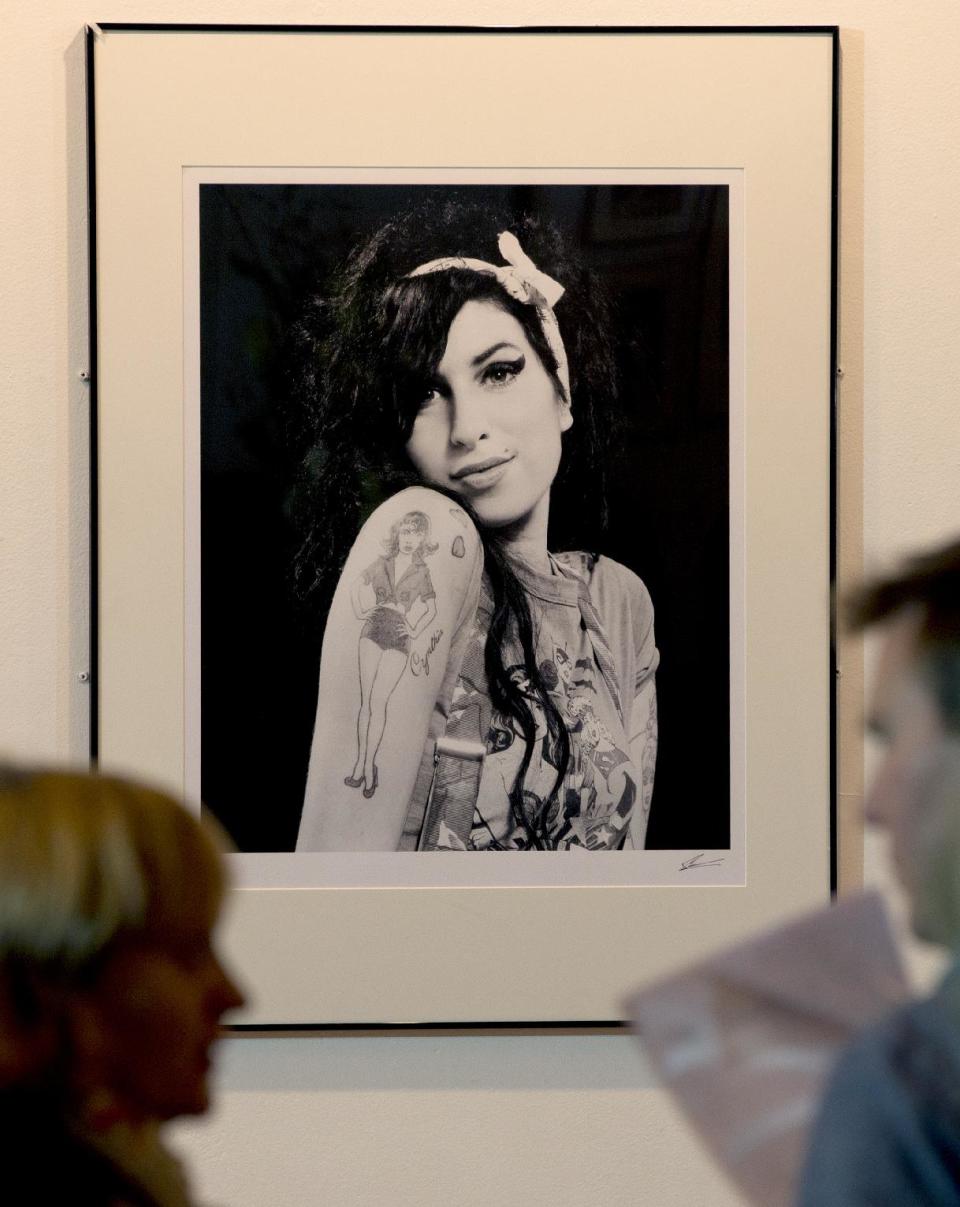 A portrait of the late British singer Amy Winehouse is looked at by members of the media at the Proud gallery in Camden, London, Wednesday, Sept.11,2013. In the month she would have turned 30, Amy Winehouse is being celebrated in Camden the London neighbourhood that was her physical and spiritual home, she died of accidental alcohol poisoning at her house in July 2011, aged 27. The neighbourhood still attracts her fans, and local officials and businesses are holding a series of September events to raise money for the Amy Winehouse Foundation, a youth charity established by the singer's family. (AP Photo/Alastair Grant)