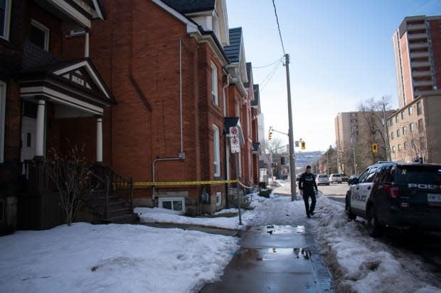 A Hamilton police officer waits beside 104 and 102 Wellington Street North in Beasley.