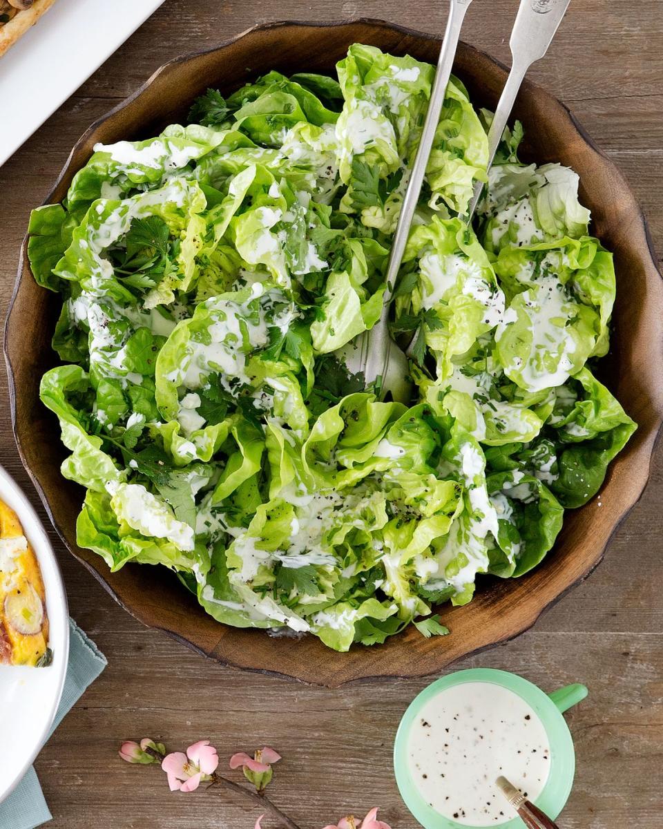 creamy bibb and herb salad in a large wooden bowl with a salad serving utensils