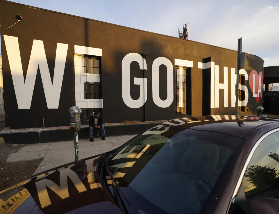 A person wears a mask as he checks his mobile phone outside the temporary closed "HVY Industry," an inclusive training gym, under a mural reading " We Got this LA," in Los Angeles Thursday, Jan. 7, 2021. A surge following Halloween and Thanksgiving produced record hospitalizations and now the most seriously ill of those patients are dying in unprecedented numbers. California health authorities reported Thursday 583 new deaths and a record two-day total of 1,042. (AP Photo/Damian Dovarganes)