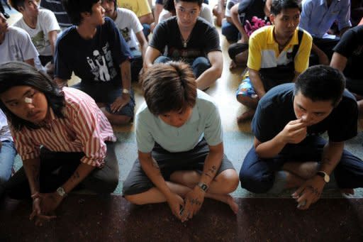Thai youths with their calling numbers written on their arms sit as they wait for the start of a selection process to pick military recruits - through a lottery system - held at a temple grounds in Bangkok