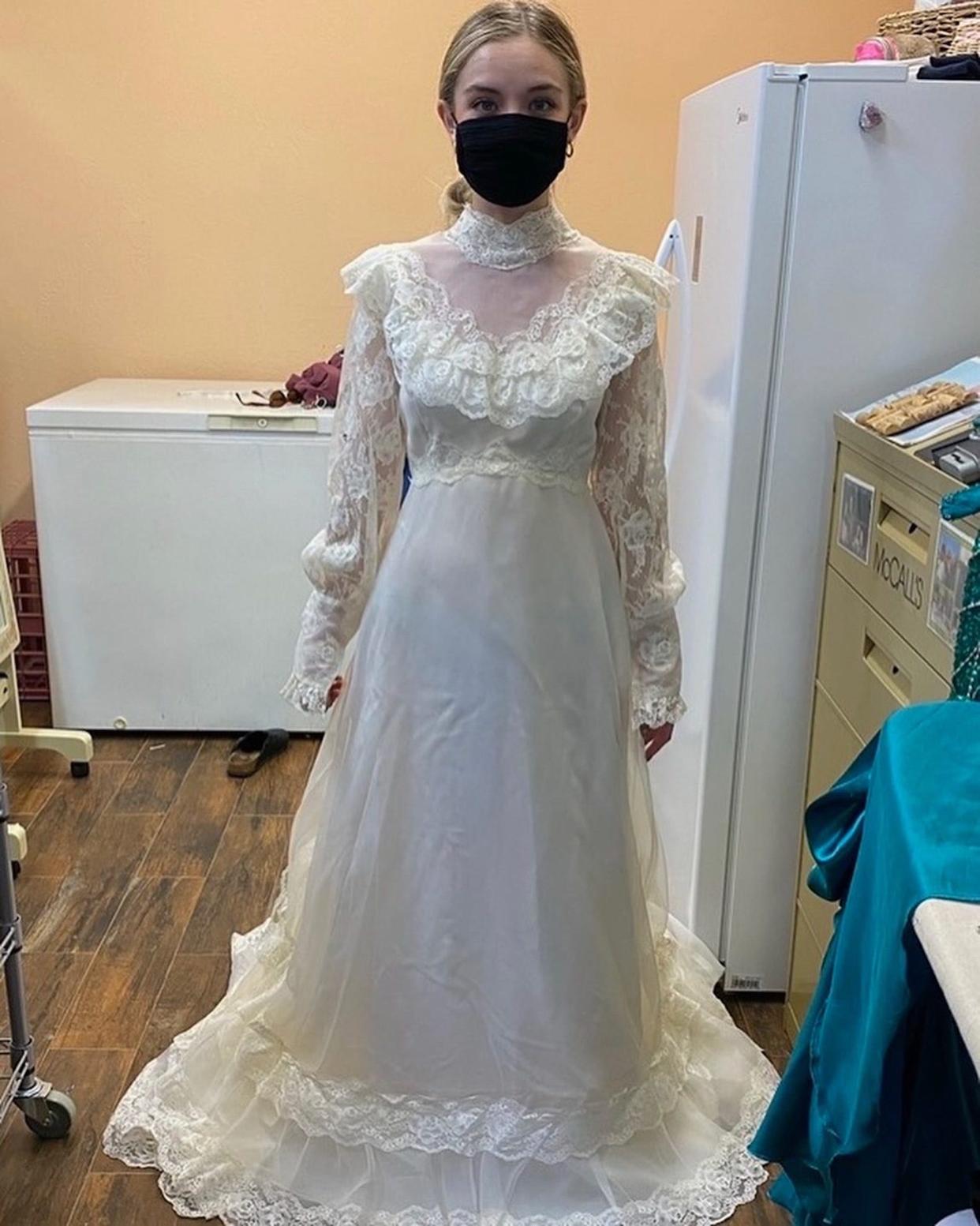 A bride stands in a longsleeve wedding dress in a seamstress shop.