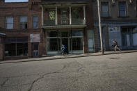 A boy rides his bicycle while a girl runs with her skateboard past abandoned storefronts along the streets of Shawnee, Ohio, on Friday, July 24, 2020. Shawnee was a coal town that once boasted an opera house, a vaudeville theater, dozens of stores and plenty of taverns. Today, Main Street is little but one abandoned building after another. (AP Photo/Wong Maye-E)