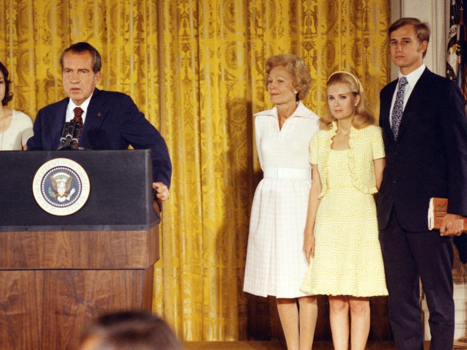 Richard Nixon at a podium next to his wife Pat in a white knee-length dress and his daughter and son.
