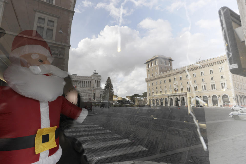 Empty Piazza Venezia Square is reflected in a window of a closed shop in Rome, Thursday, Dec. 24, 2020. Italians are easing into a holiday season full of restrictions, and already are barred from traveling to other regions except for valid reasons like work or health. Starting Christmas eve, travel beyond city or town borders also will be blocked, with some allowance for very limited personal visits in the same region. (AP Photo/Gregorio Borgia)