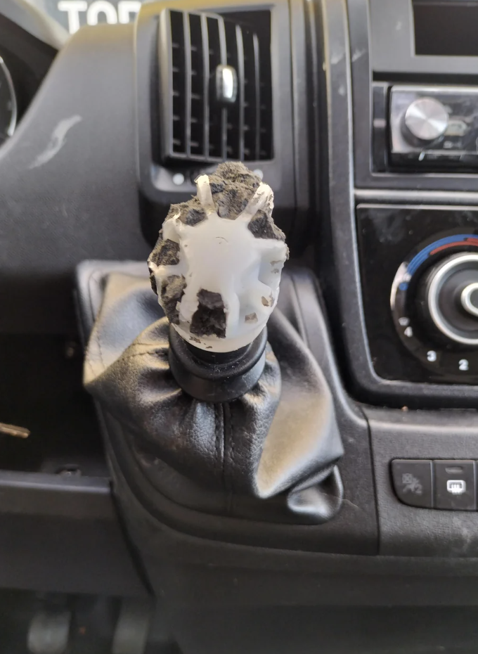 A worn gear shift knob with multiple surfaces missing, revealing the white material underneath