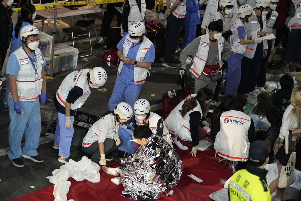 Rescue workers treat injured people on the street near the scene where scores of people died and were injured in Seoul, South Korea, Sunday, Oct. 30, 2022. Witnesses say the nightmarish scene intensified as people performed CPR on the dying and carried limp bodies to ambulances, while dance music pulsed from garish clubs lit in bright neon. Others tried desperately to pull out those who were trapped underneath the crush of people, but failed because too many in the crowd had fallen on top of them. (AP Photo/Lee Jin-man)