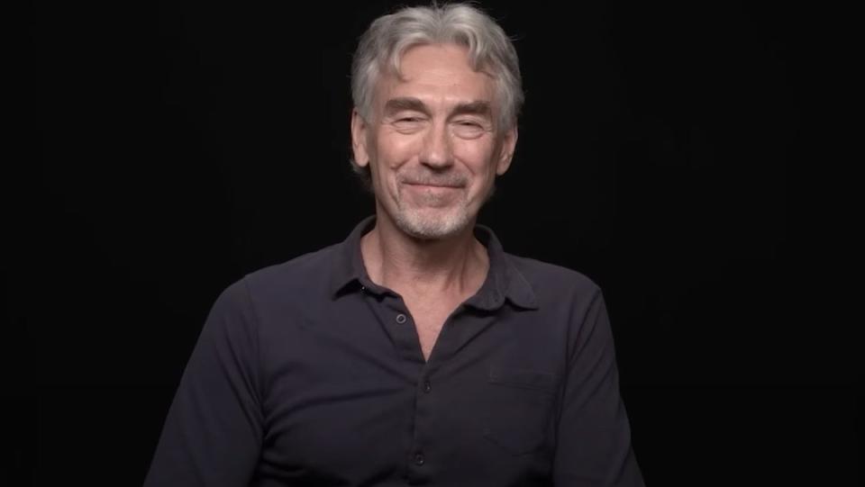 Tony Gilroy smiles sititng in front of a black background