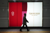A man wearing a protective mask to help curb the spread of the coronavirus walks near a banner of the Tokyo 2020 Olympics at an underpass in Tokyo Tuesday, Jan. 19, 2021. The Tokyo Olympics are to open in six months on July 23. Interestingly, Tokyo organizers have no public program planned to mark the milestone. There is too much uncertainty for that right now. (AP Photo/Eugene Hoshiko)