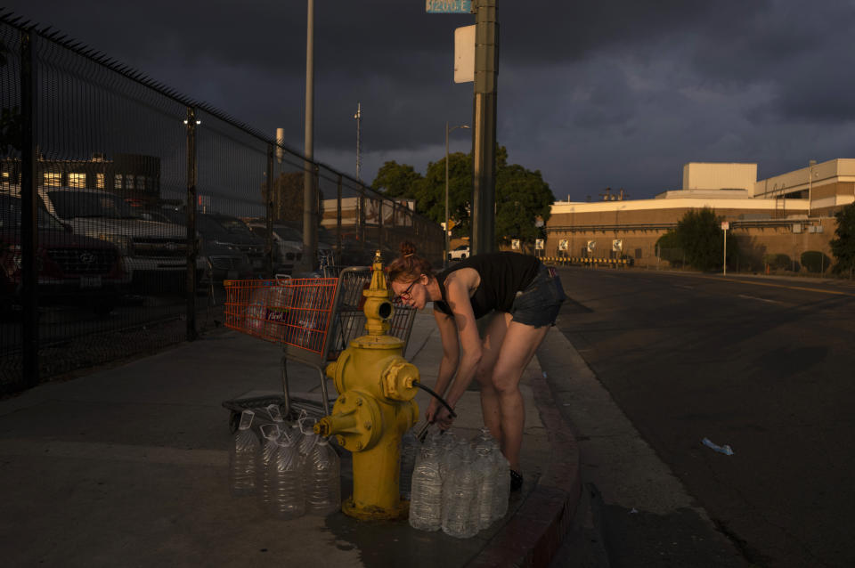 Victoria Filipy, who lives in a small homeless RV encampment with her dogs, fills water bottles from a fire hydrant in Los Angeles, Wednesday, Oct. 25, 2023. (AP Photo/Jae C. Hong)