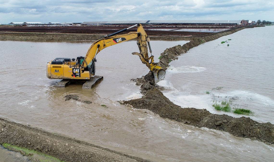 An excavator works to build a diversion berm to keep floodwater from a dairy in Kings County south of Hanford on Thursday, March 23, 2023.