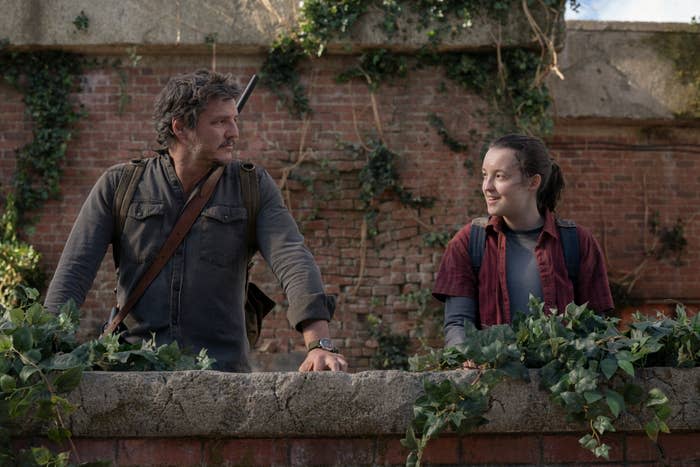 Pedro Pascal and Bella Ramsey in "The Last of Us" as Joel and Ellie, standing by a wall with foliage