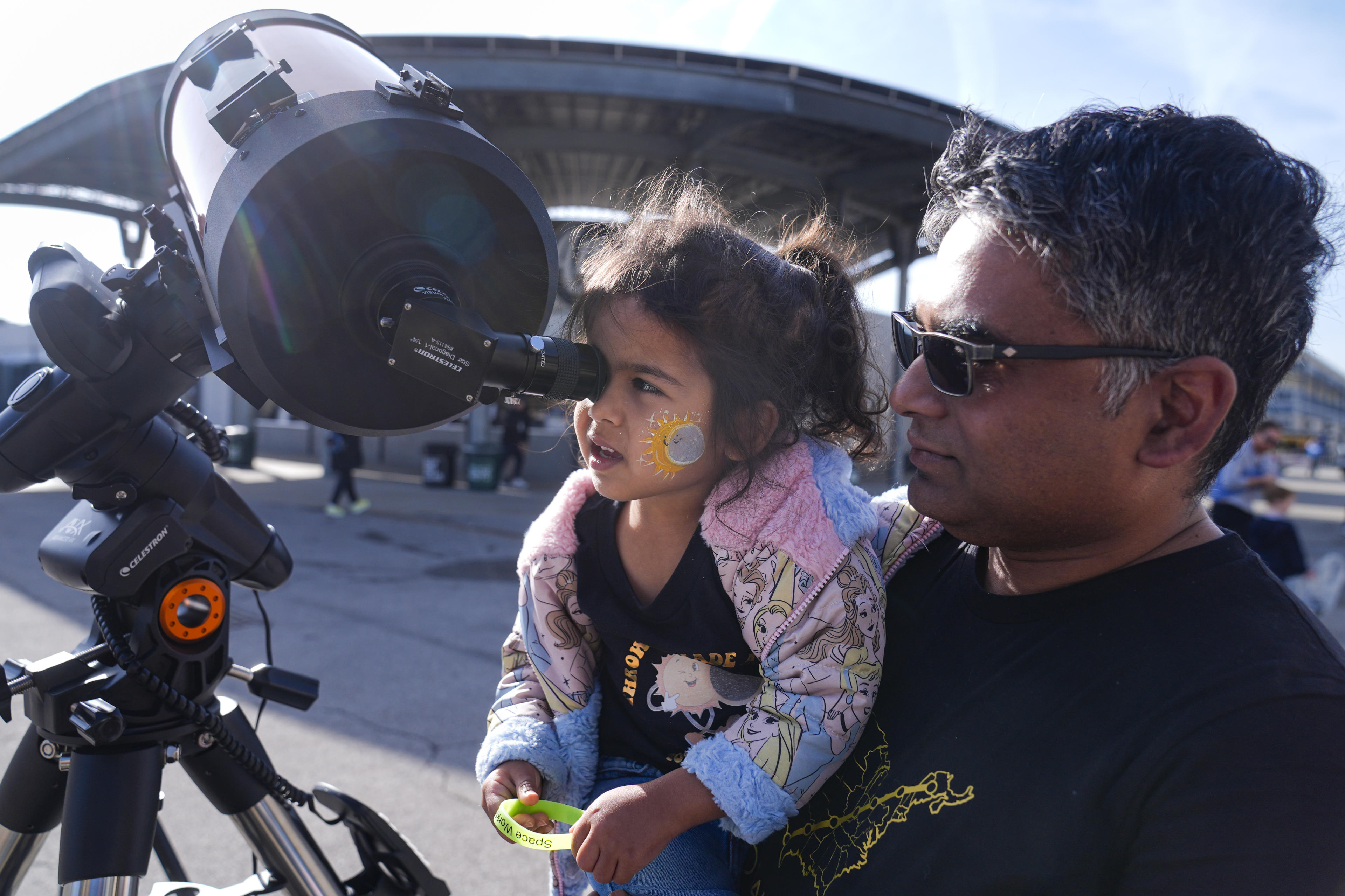 Tawhid Rana, of Midland, Mich., hold his daughter Thia, as she views the sun through a telescope at the Indianapolis Motor Speedway in Indianapolis, Monday, April 8, 2024. (Michael Conroy/AP)