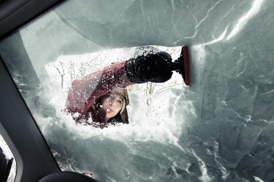 woman cleaning snow from car's windshield