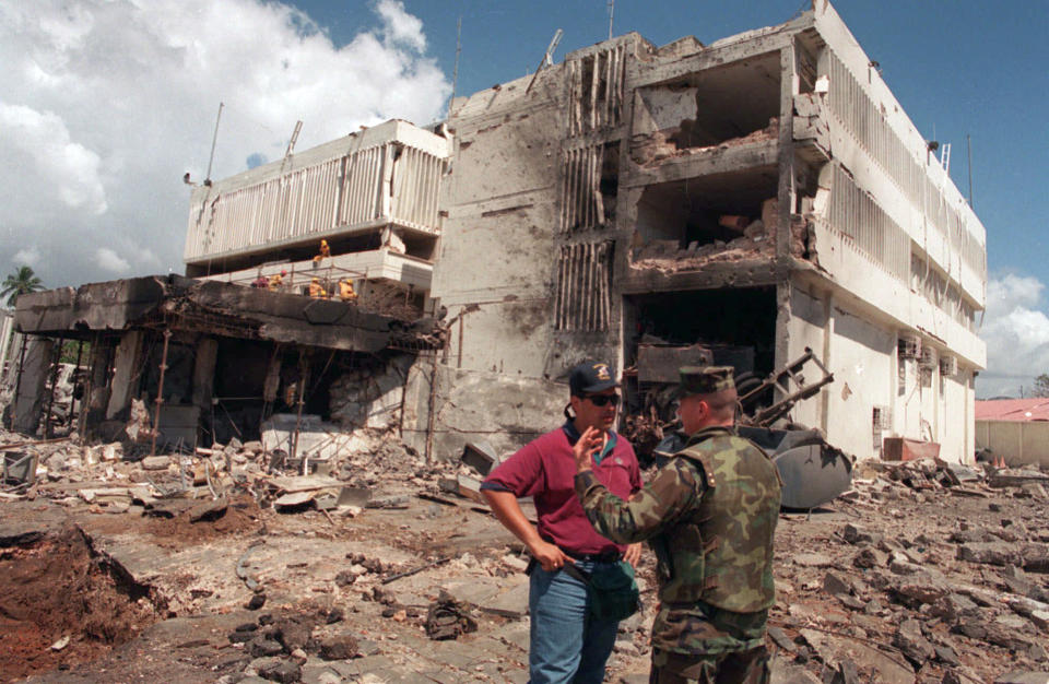 FILE - In this Aug. 15, 1998 file photo, a U.S. Marine talks with an FBI investigator in front of the damaged U.S. embassy in the capital Dar es Salaam, Tanzania. In 1996, Osama bin Laden issued a formal declaration of war. But it wasn't until trucks loaded with explosives detonated outside of U.S. embassies in Nairobi, Kenya, and Dar es Salaam, killing more than 200 people on Aug. 7, 1998, that the threat became real. (AP Photo/Brennan Linsley, File)