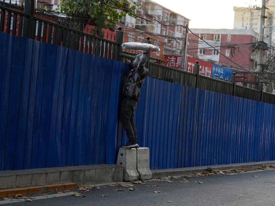 A man retrieves an item through the fences around a Beijing community under lockdown.