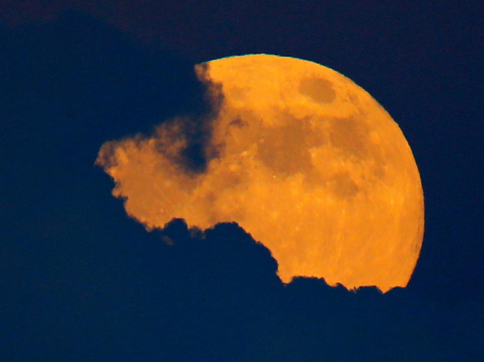 An orange moon partly covered by dark clouds.