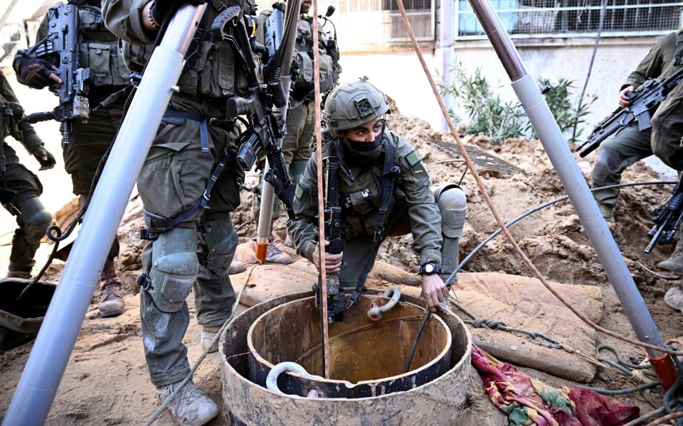 The soldiers stand around the mouth of a shaft, with one feeding in a cable