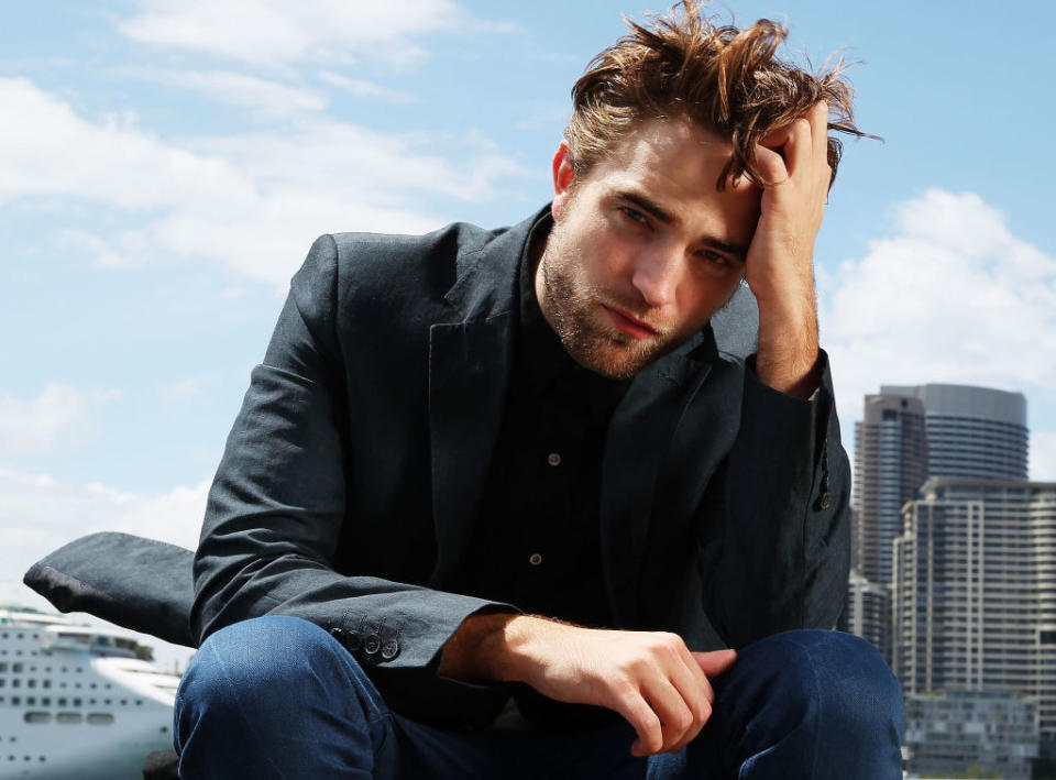 Robert Pattinson sitting with his hand in his hair