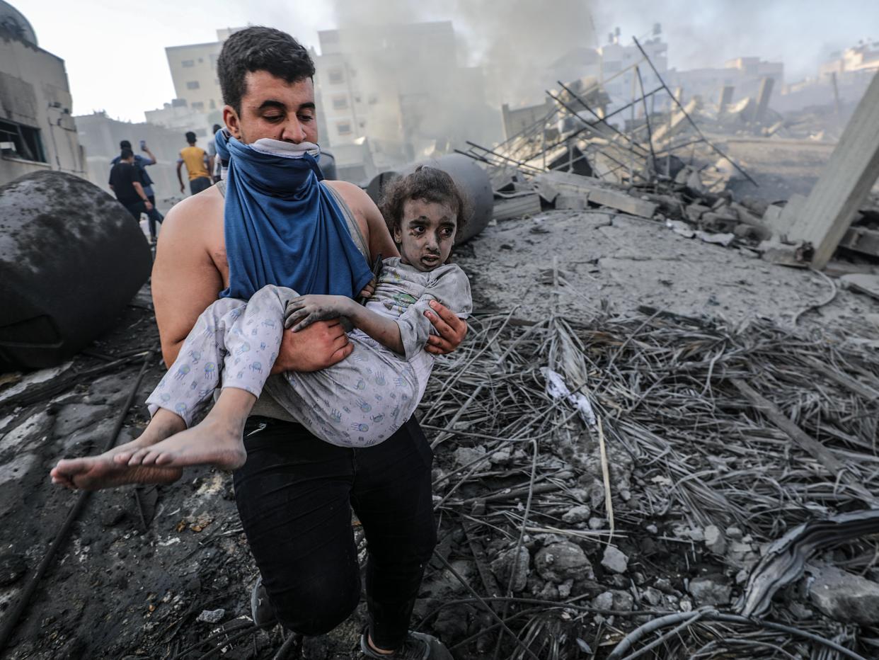 A Palestinian man carries a wounded girl after recovering her from the rubble (EPA)