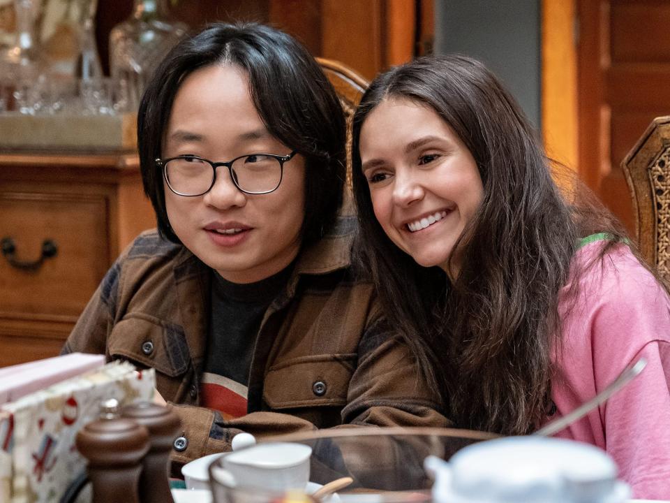 Jimmy O. Yang and Nina Dobrev sitting next to each other at a dining table in "Love Hard."