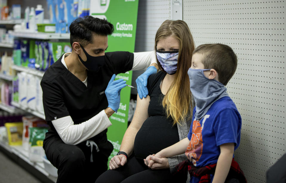 This photo provided by Chorus Media Group, Skippack Pharmacy owner and pharmacist Dr. Mayank Amin administers vaccine to Aubrie Cusumano while son, Luca looks on Feb. 11, 2021, in Skippack, Pa. In communities across the country, local pharmacy owners are among the people administering COVID-19 vaccinations. Being a vaccine provider requires a big investment of time and paperwork, and for some, finding a location for a mass vaccination clinic. (Chorus Media Group via AP)