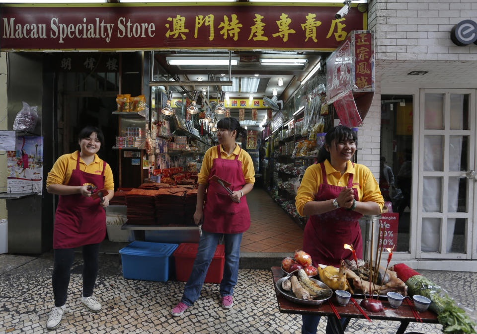 In this Feb. 1, 2014 photo, shop clerks place the offering to the God in front of a local product shop during a Chinese New Year celebration in Macau. The annual holiday is the busiest time of year for the former Portuguese colony, which became a special Chinese region in 1999. Many of the millions of mainland Chinese on the move during the holiday, often referred to as the world’s biggest migration, head to Macau during the festival. (AP Photo/Vincent Yu)