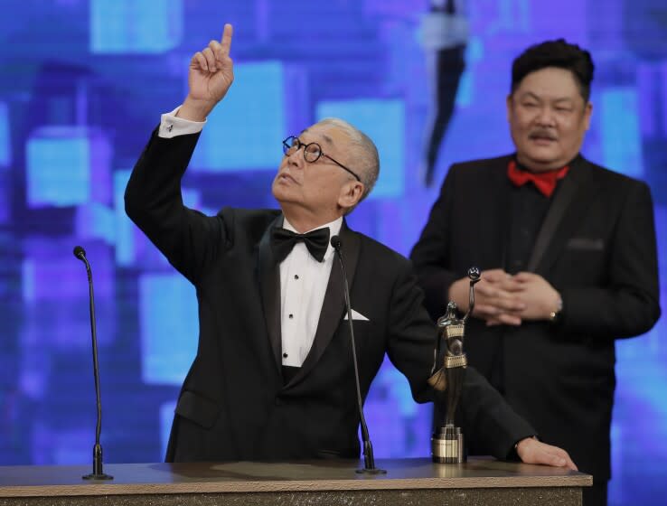 A man in a tuxedo standing behind a podium and pointing up to the sky