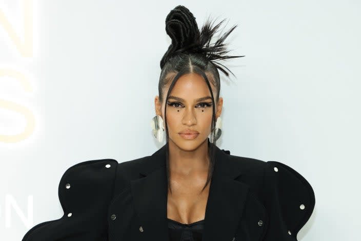 Cassie Ventura poses in an avant-garde blazer with unique wavy sleeves and silver studs over a bandeau top and matching pants