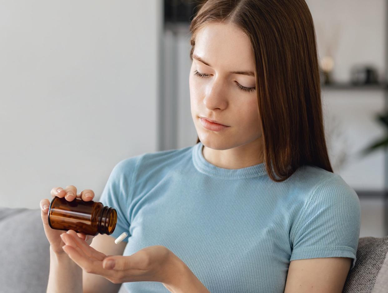 Young woman hold bottle of capsules prepare to swallow pill, taking meds. Sick female drink painkiller or antidepressant