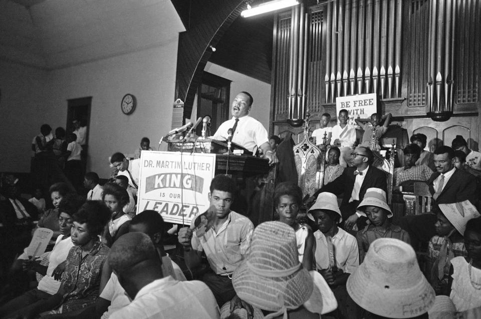 Dr. Martin Luther King speaks at rally at African American church in St. Augustine, Florida June 11, 1964, as sign hangs from podium reading “Dr. Martin Luther King is our leader” before march on downtown old slave market. In foreground are African Americans just released from jail arrested for demonstrations last week. The Associated Press