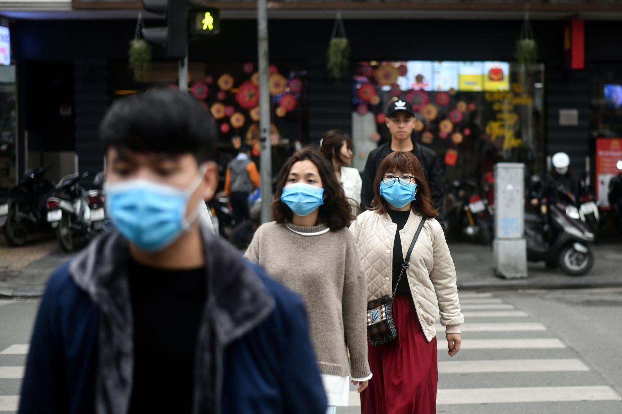 Pedestrians, wearing protective facemasks amid concerns of the novel coronavirus outbreak, cross a street in Hanoi on February 7, 2020. (Photo by Manan VATSYAYANA / AFP) (Photo by MANAN VATSYAYANA/AFP via Getty Images)