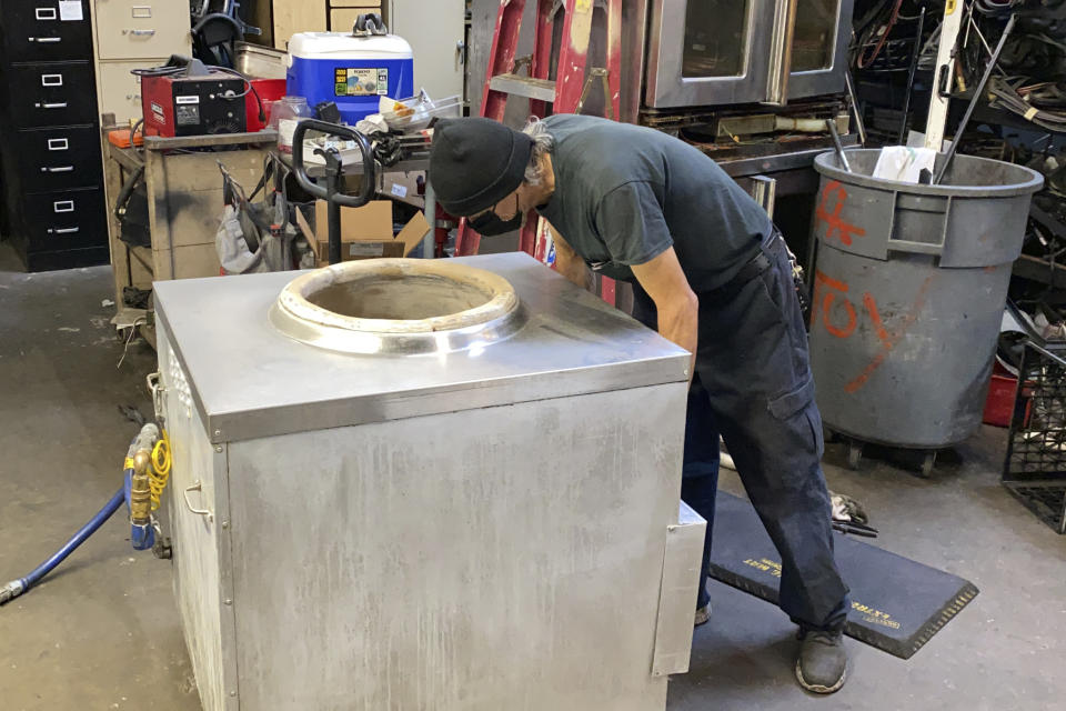 An employee fixes a used appliance for sale inside the warehouse of American Restaurant Supply, which is packed with appliances and furniture from restaurants that have shut down during the pandemic, in San Leandro, Calif., on Jan. 14, 2021. The pandemic has forced thousands of restaurants to permanently shut their doors as dining restrictions keep customers away. But the unprecedented closures have created a business boom for commercial auctioneers that buy and sell used restaurant equipment. (AP Photo/Terry Chea)