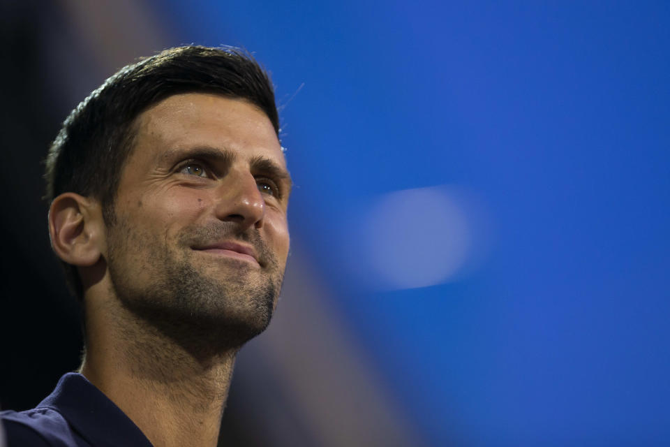 Novak Djokovic smiling ad watching a tennis match.