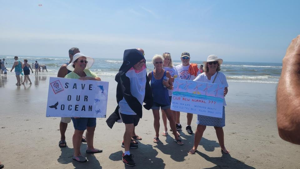 Participants in "Hands Across the Beaches" on July 15 stand on the Ocean City beach with signs protesting offshore windmill farming in New Jersey.