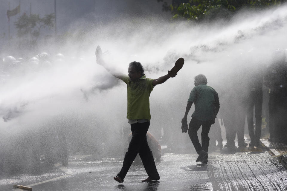 A supporter of Sri Lanka's main opposition holds his shoes in hands as police fire water cannons to disperse them during a protest rally against high taxes and increases in electricity and fuel charges, in Colombo, Sri Lanka, Tuesday, Jan. 30, 2024. (AP Photo/Eranga Jayawardena)