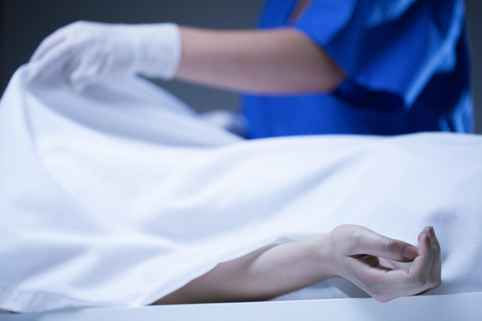 Worker of morgue covering corpse by sheet